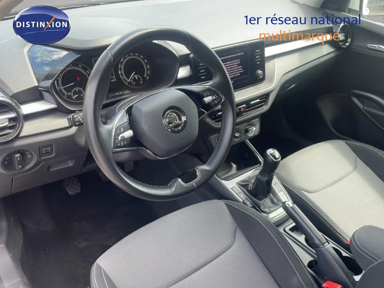 Vue intérieure centrée sur le volant cuir et la console centrale avec levier de vitesse manuelle d'une Skoda Fabia blanche.