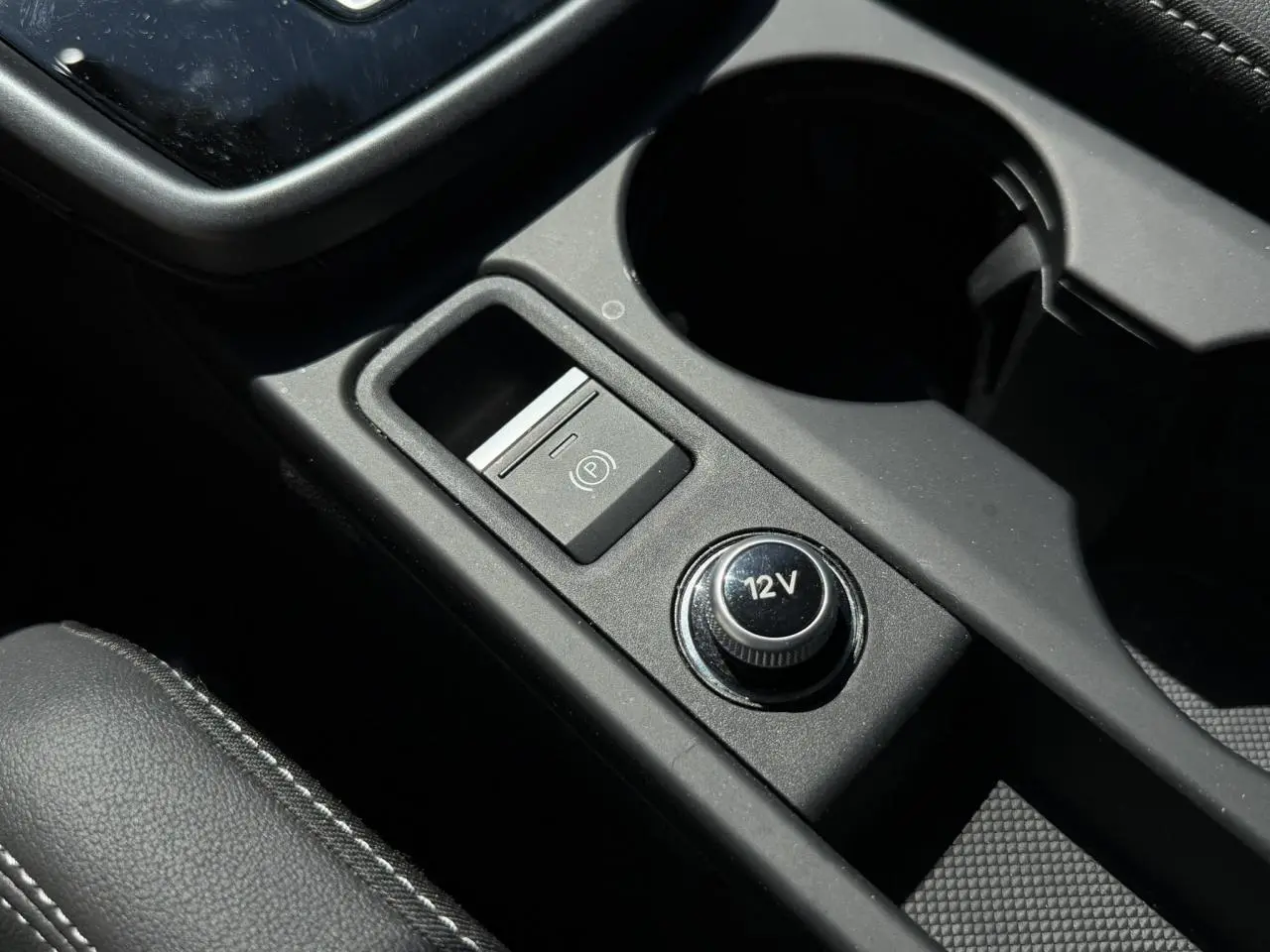 Gros plan sur la console centrale noire de l'Audi A3 Sportback 2025, avec bouton 12V et frein à main électrique.