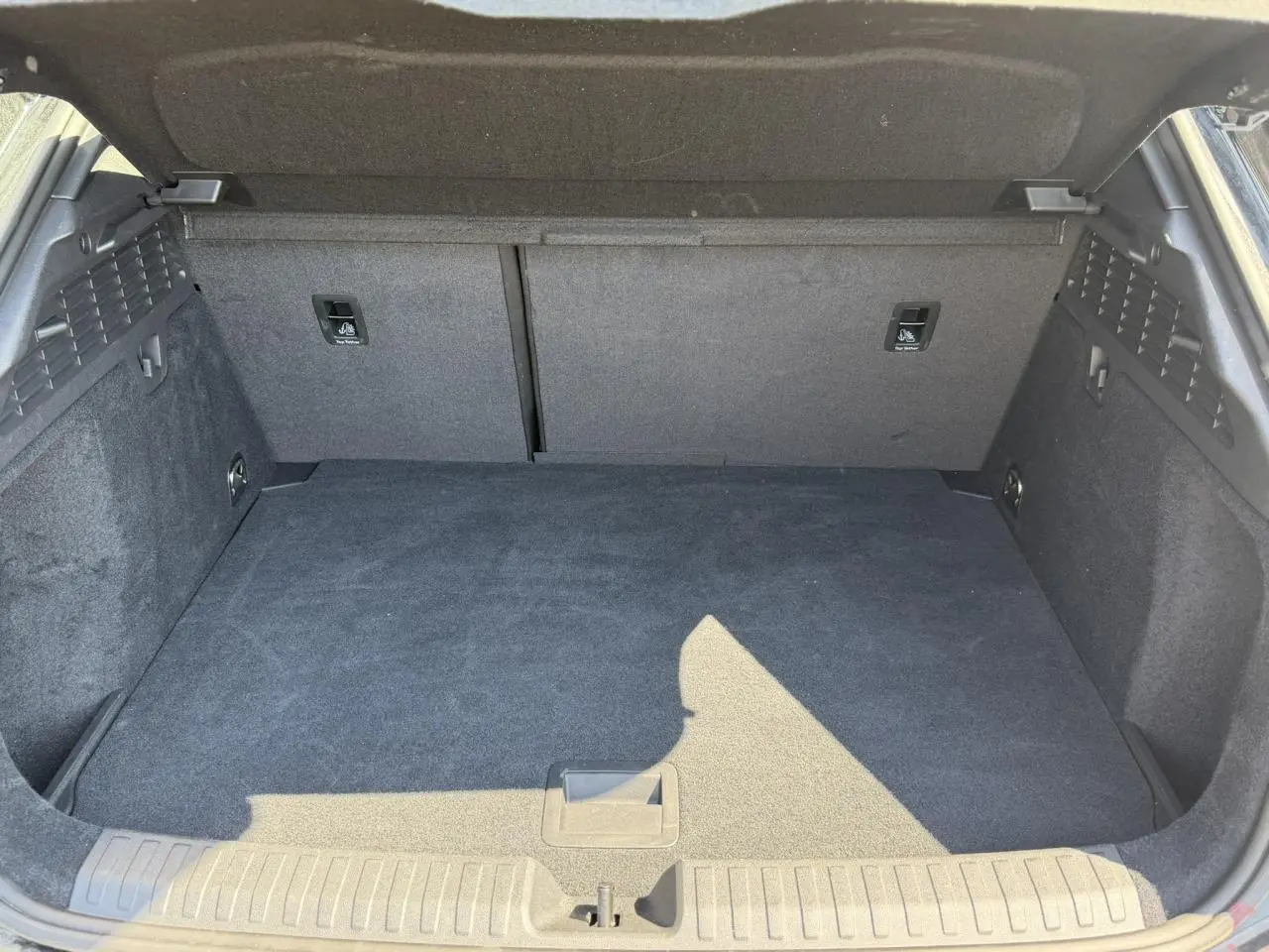 Coffre ouvert vu de l'arrière d'une Audi A3 Sportback noir Mythe, espace de chargement vide et tapis gris foncé.