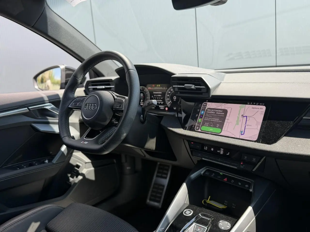 Vue intérieure côté conducteur de l'Audi A3 Sportback 2025, volant cuir noir et écran tactile de navigation allumé.
