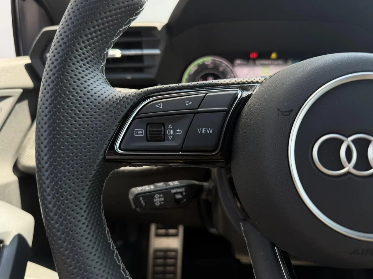 Gros plan sur le volant perforé noir de l'Audi A3 Sportback 2025, avec commandes multifonctions côté gauche.