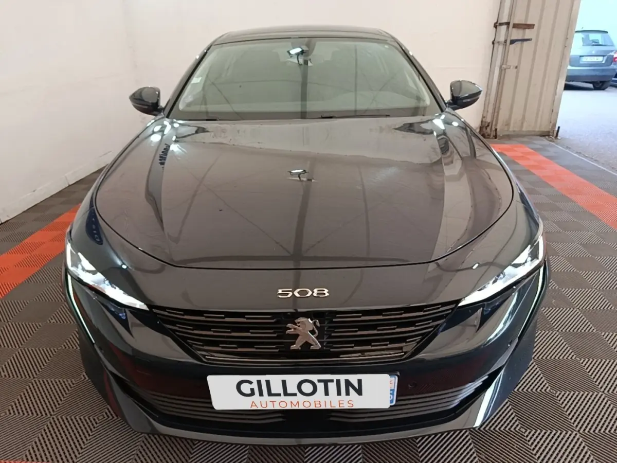 Vue frontale d'une Peugeot 508 gris foncé avec calandre noire et feux LED allumés dans un garage.
