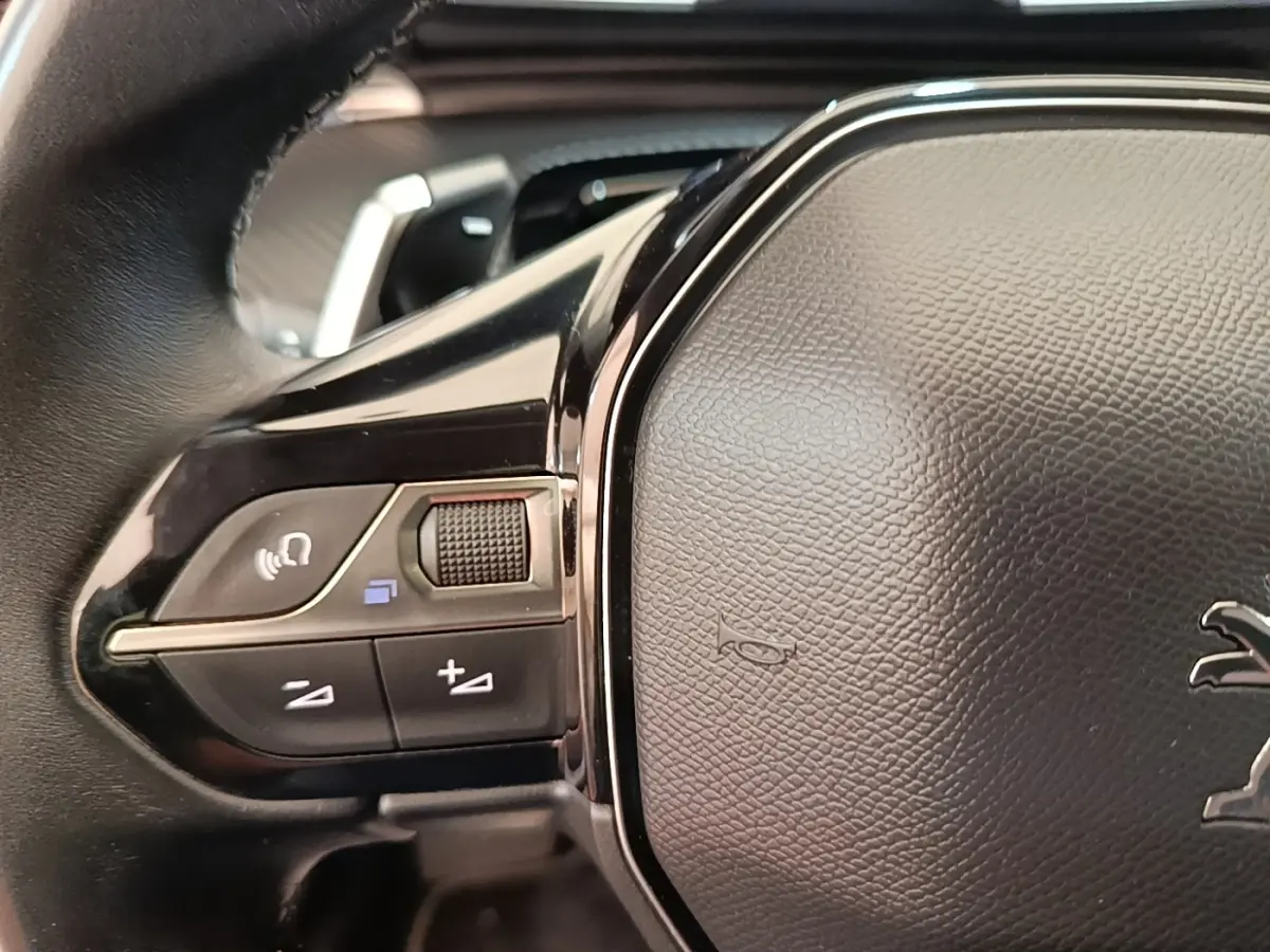 Gros plan sur le volant cuir noir de la Peugeot 508 gris foncé, avec commandes audio intégrées à gauche.