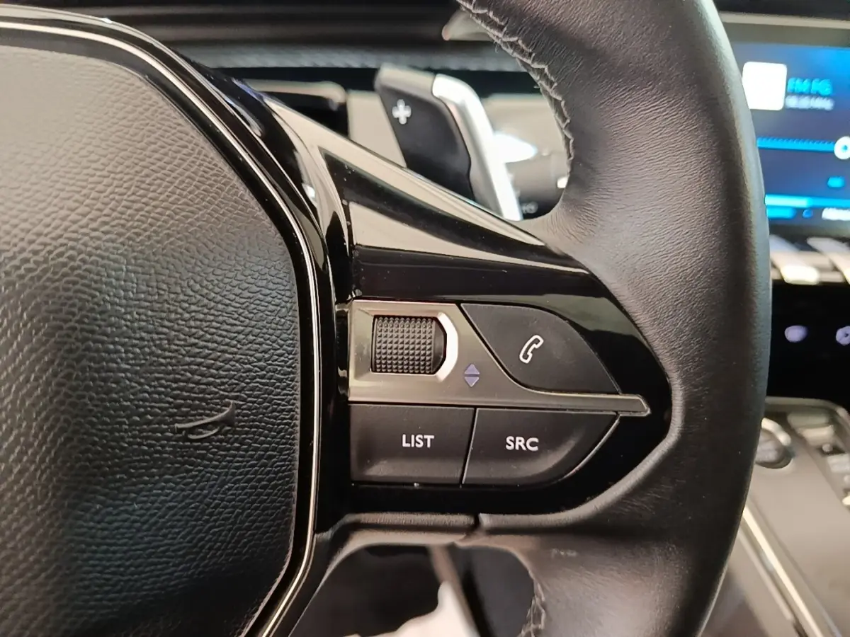 Gros plan sur le volant cuir noir de la Peugeot 508 Puretech 180, avec commandes audio et téléphone intégrées.