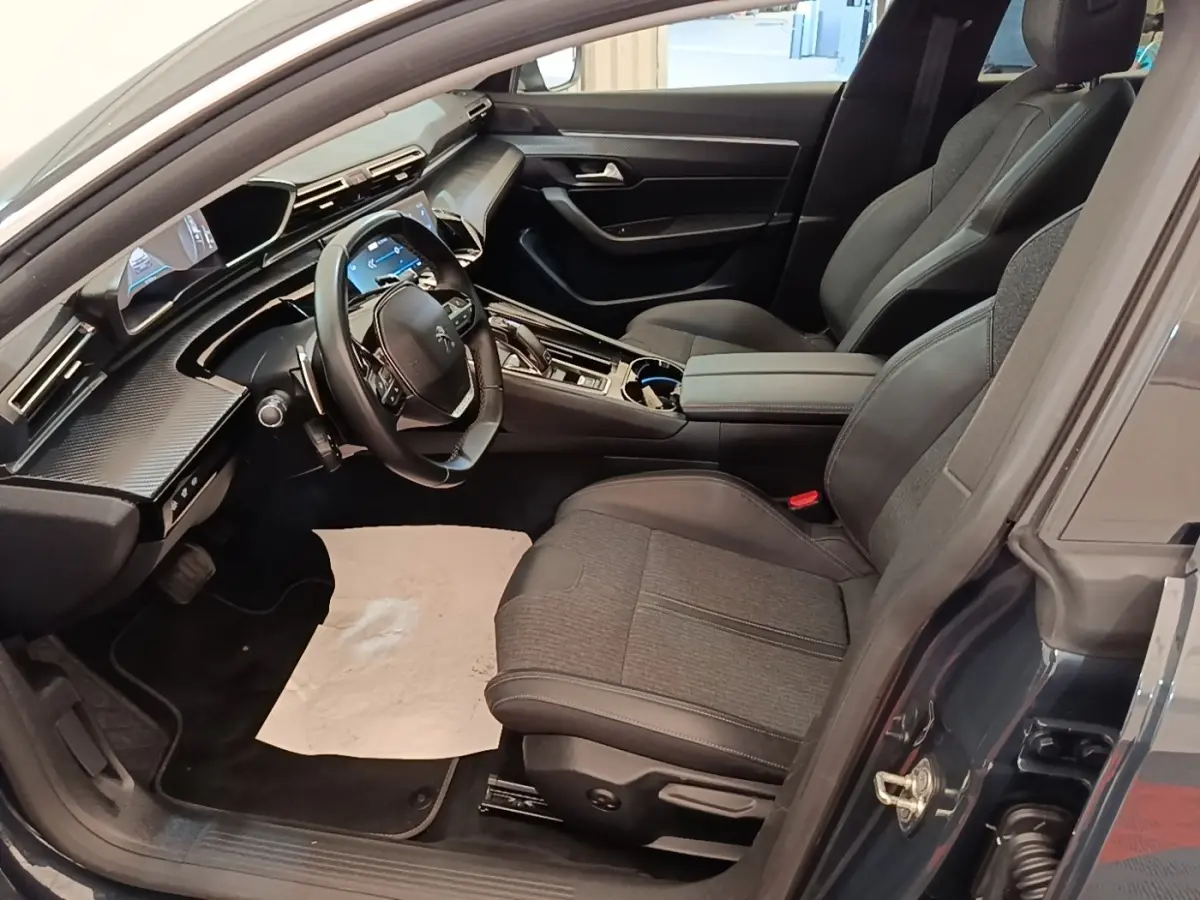 Vue intérieure côté conducteur de la Peugeot 508 gris foncé, mettant en valeur le tableau de bord numérique et les sièges en tissu et cuir.