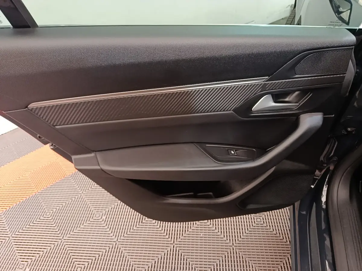 Vue intérieure côté gauche de la porte avant d’une Peugeot 508 gris foncé avec insert carbone et poignée argentée.