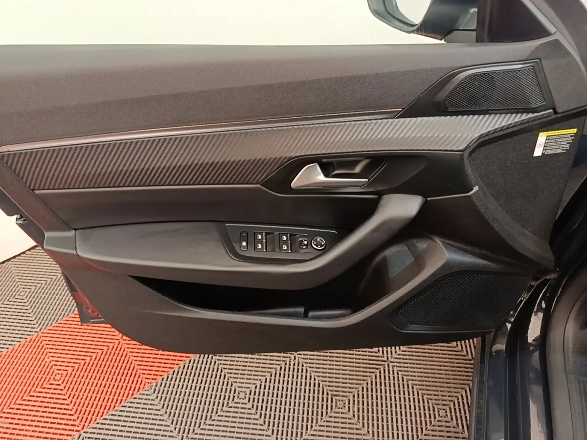 Vue rapprochée de la porte avant gauche de la Peugeot 508 gris foncé, avec garniture carbone et commandes électriques.