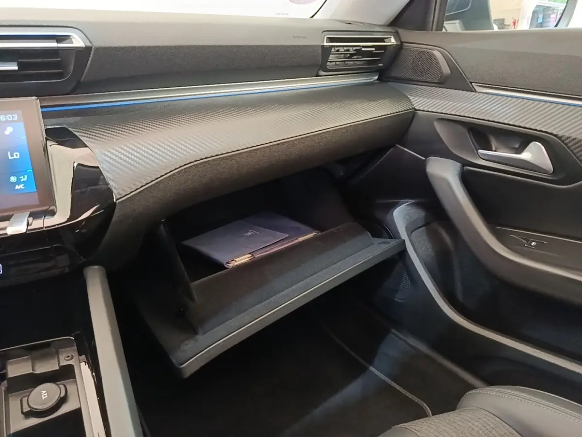 Intérieur de la Peugeot 508 gris foncé, vue côté passager avec boîte à gants ouverte et tableau de bord moderne.