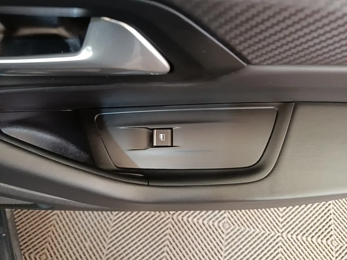 Détail de la commande de lève-vitre côté conducteur sur la porte intérieure noire d'une Peugeot 508 gris foncé.