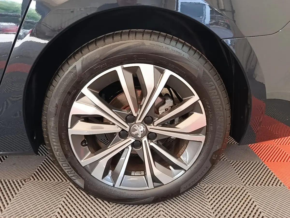 Gros plan sur la roue avant droite d’une Peugeot 508 gris foncé avec jante alliage au design moderne.