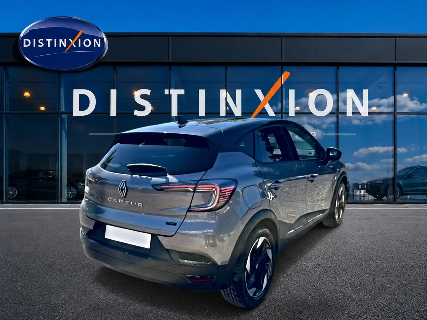 Vue 3/4 arrière droite d'un Renault Captur gris cassiopée 2026 devant une vitrine Distinxion, jantes noires et feux LED.