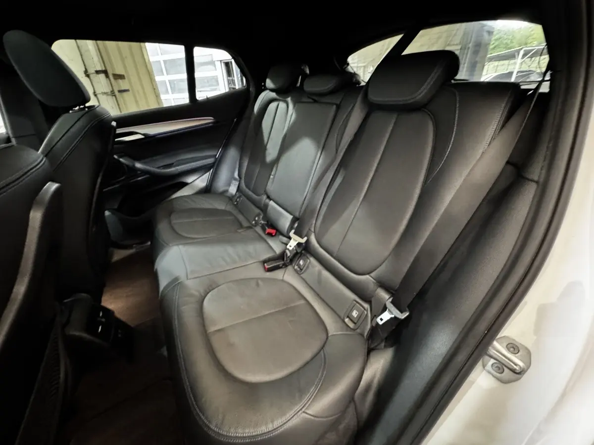 Vue intérieure côté droit montrant la banquette arrière en cuir noir d'une BMW X2 blanche, avec ceinture de sécurité visible.