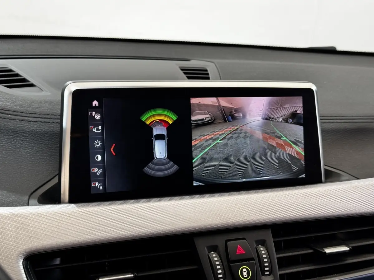 Écran central du BMW X2 blanc montrant la caméra de recul et l’alerte de proximité en stationnement.