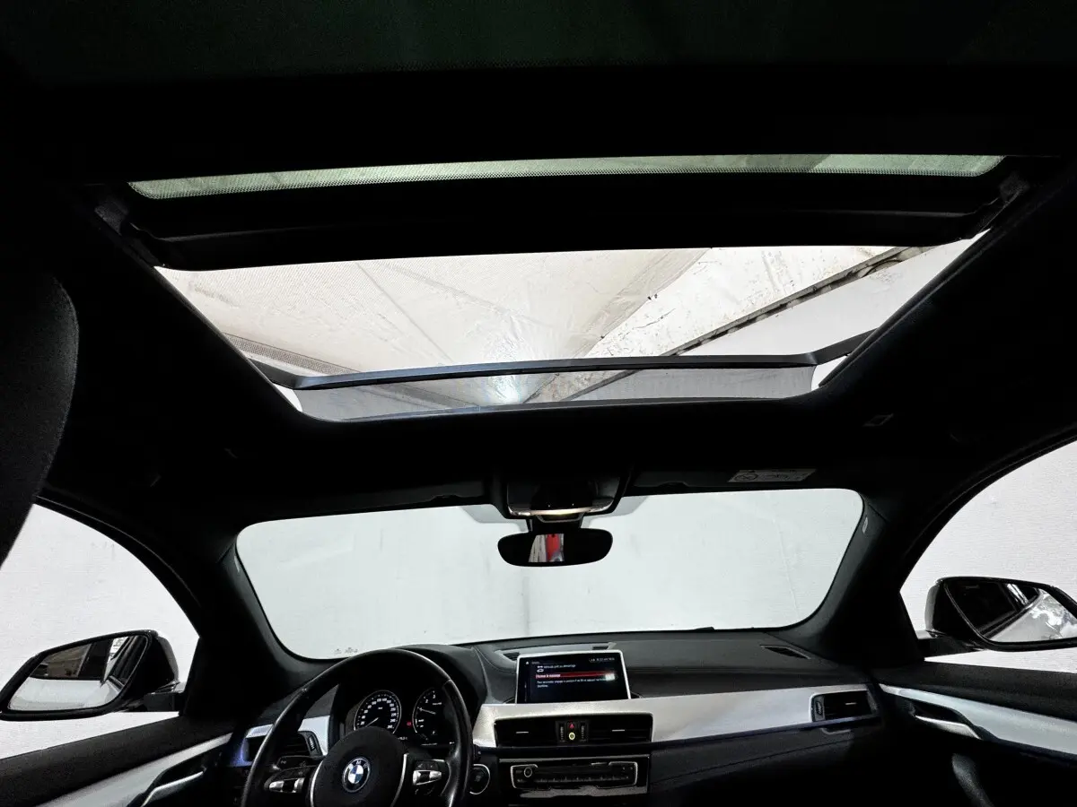 Vue intérieure avant du BMW X2 blanc xDrive25e M Sport 2022, avec toit panoramique et tableau de bord moderne.