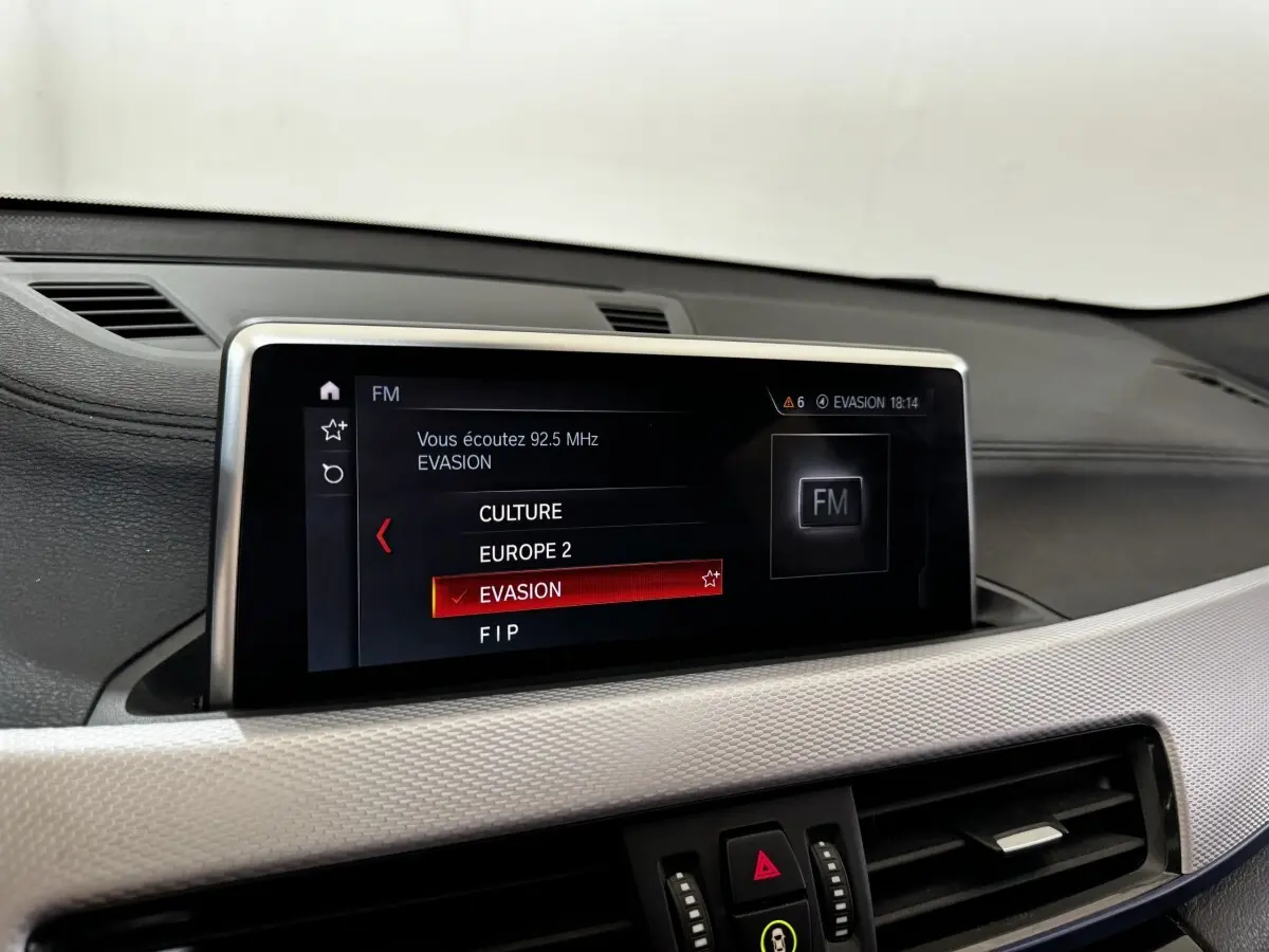 Écran central tactile du tableau de bord du BMW X2 blanc, affichant la radio FM sur la station Evasion.