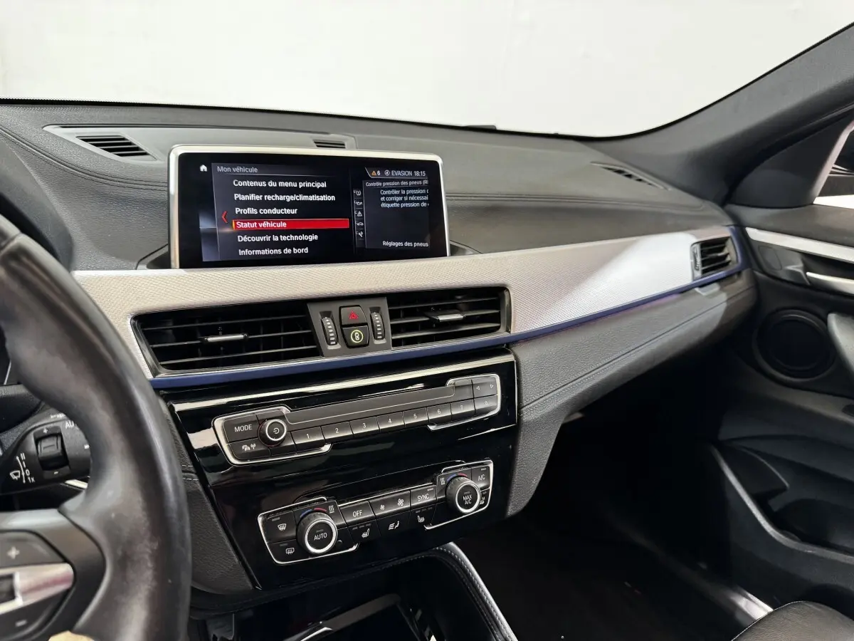Intérieur BMW X2 xDrive25e 2022 vu côté conducteur, tableau de bord avec écran central et commandes climatisation.