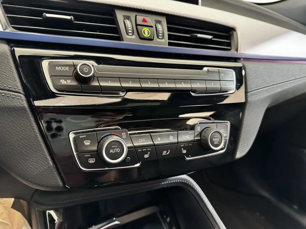 Gros plan sur la console centrale noire brillante du BMW X2 xDrive25e M Sport 2022, avec commandes climatisation et multimédia.