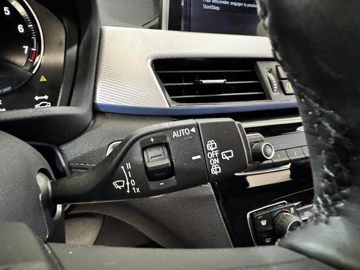 Gros plan sur la commande d’essuie-glace à gauche du volant dans l’habitacle noir et gris du BMW X2 blanc.
