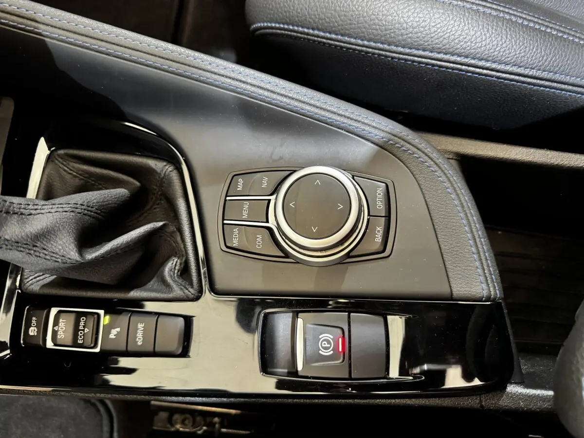Gros plan sur la console centrale noire du BMW X2 blanc, avec molette de navigation et levier de vitesse cuir.