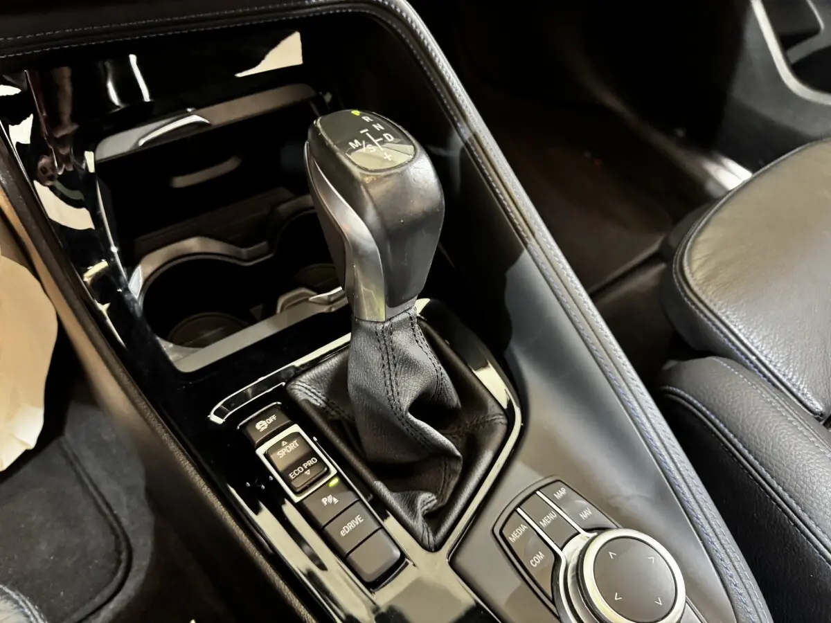 Gros plan sur la console centrale noire du BMW X2 blanc, mettant en valeur le levier de vitesse et les commandes multimédia.