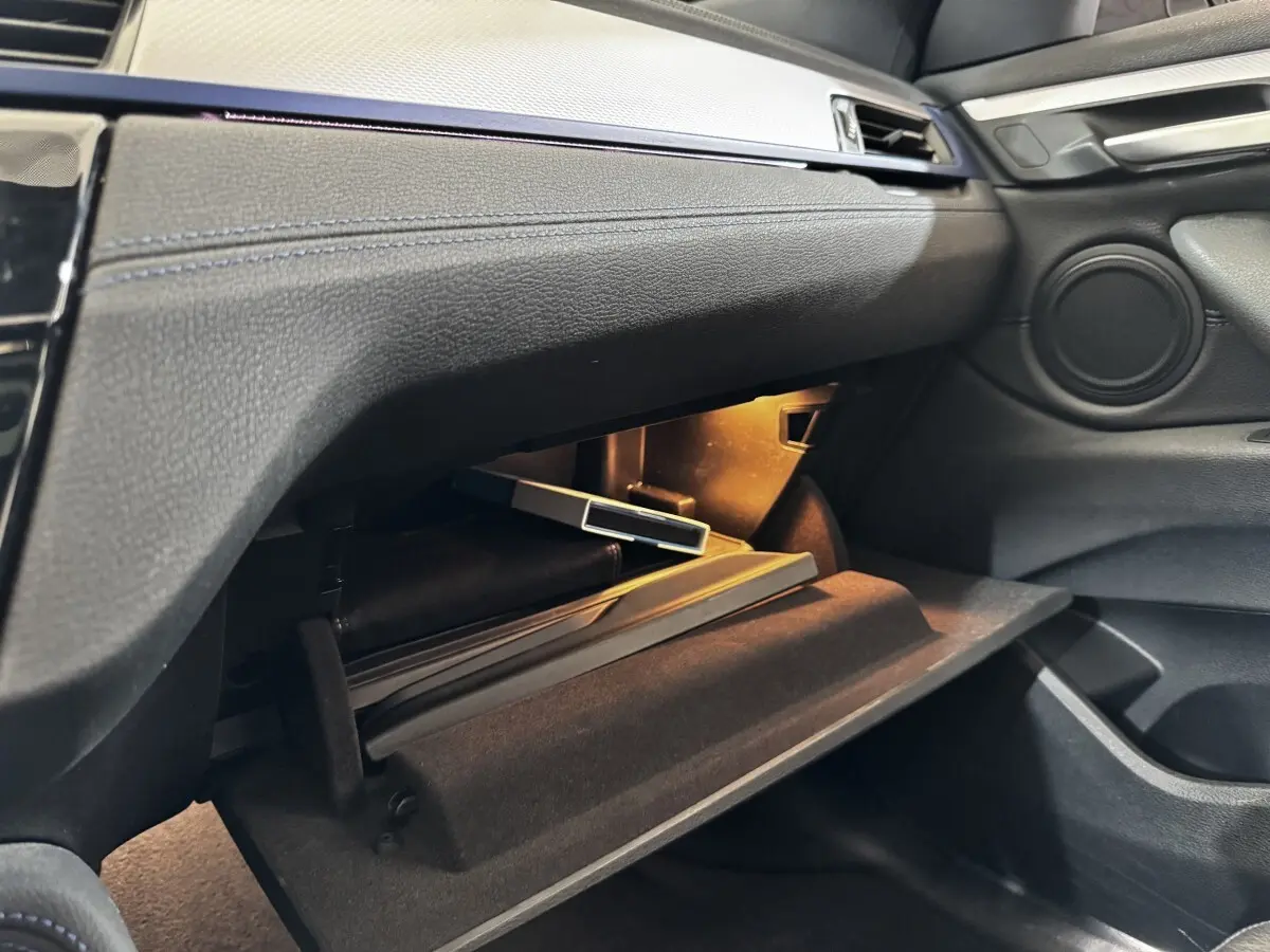 Intérieur BMW X2 xDrive25e 2022, vue côté passager sur boîte à gants ouverte avec éclairage intérieur.