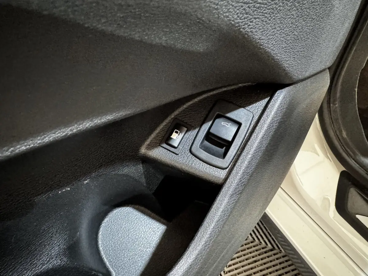 Détail des commandes d’ouverture du coffre et de la trappe à carburant sur la porte côté gauche d’un BMW X2 blanc.