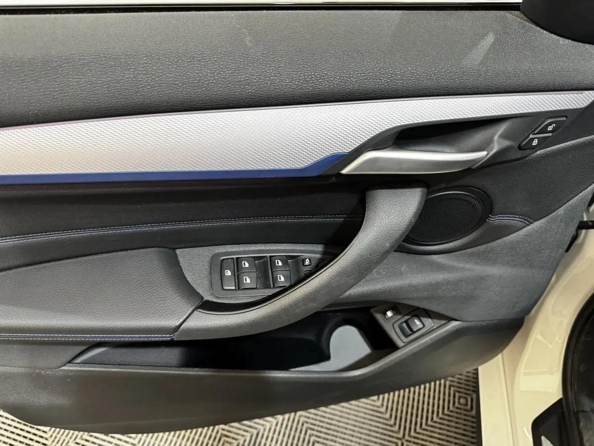 Détail de la porte avant gauche d’une BMW X2 blanche 2022, avec commandes des vitres et poignée alu.