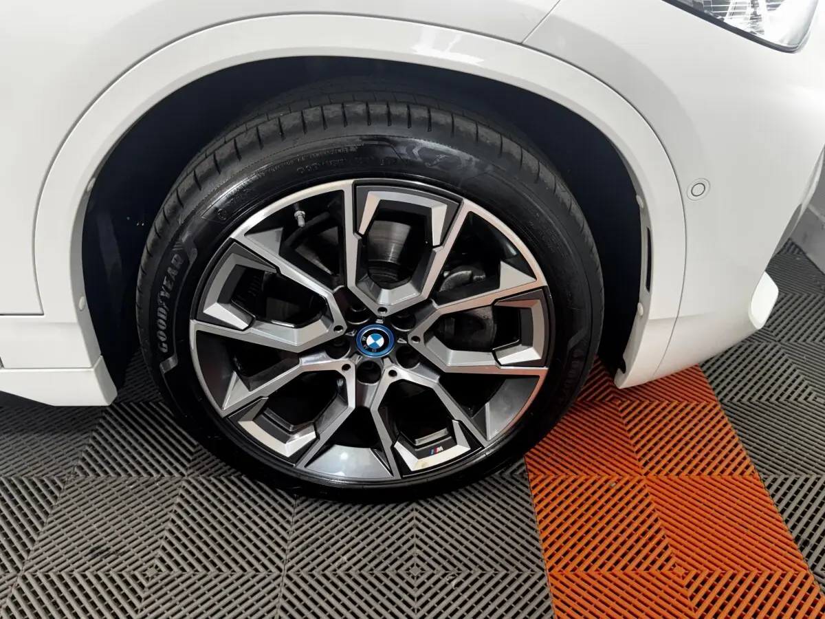 Gros plan sur la roue avant droite d’un BMW X2 blanc, jante alliage M sport avec logo coloré au centre.