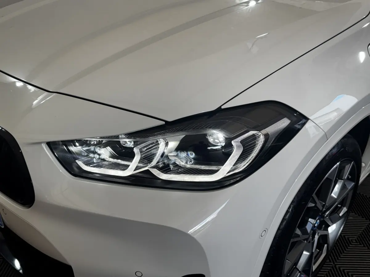 Gros plan sur le phare avant droit blanc d'un BMW X2 xDrive25e M Sport 2022 avec jante alliage visible.