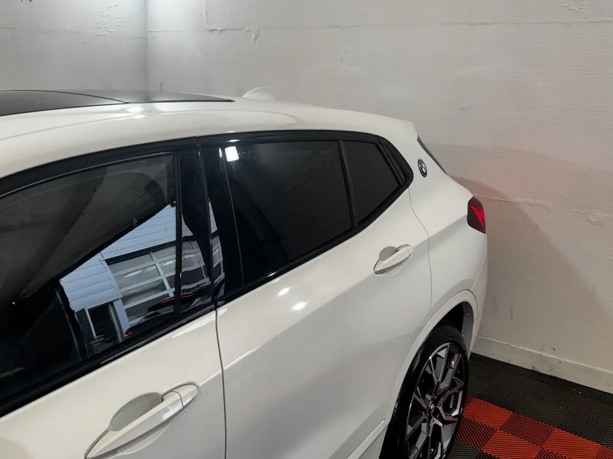 Vue côté droit arrière d'un BMW X2 xDrive25e blanc avec vitres teintées et jantes alliage distinctives.