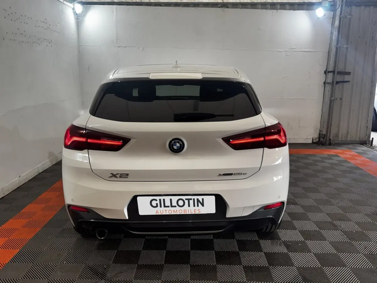 Vue arrière d'un BMW X2 blanc xDrive25e M Sport 2022 avec feux LED allumés dans un garage.