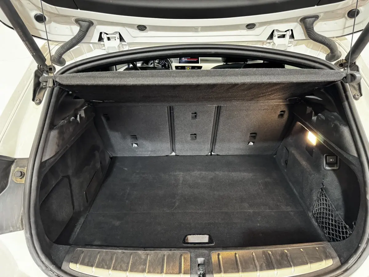 Coffre ouvert d’un BMW X2 blanc, vue intérieure montrant la banquette arrière rabattable et la protection aluminium des seuils.