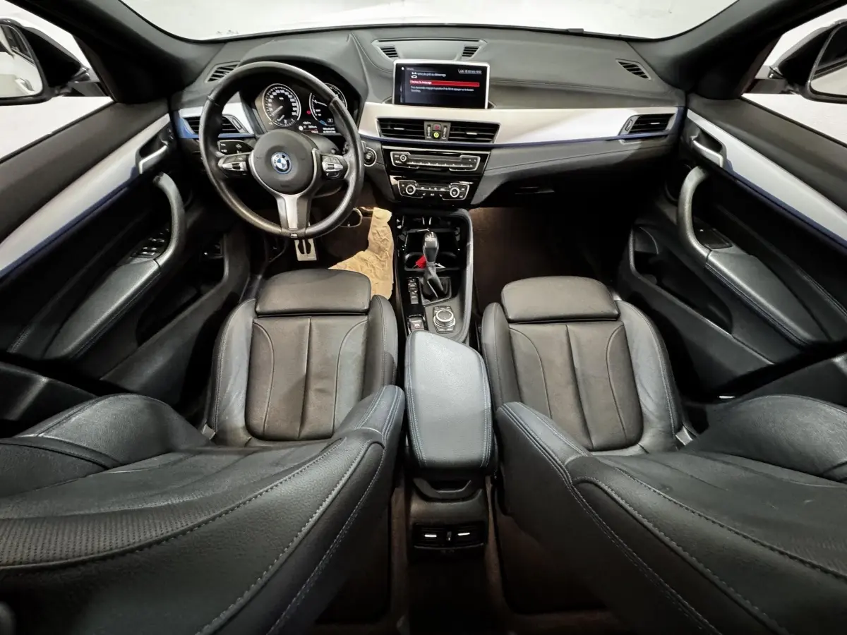 Vue intérieure avant de la BMW X2 xDrive25e M Sport 2022, sièges cuir noirs et tableau de bord avec écran central.