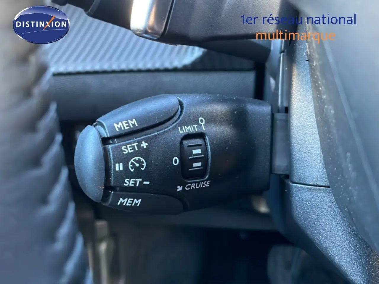 Gros plan sur la commande de régulateur de vitesse noire à gauche du volant dans une Peugeot 208 noire hybride 2025.