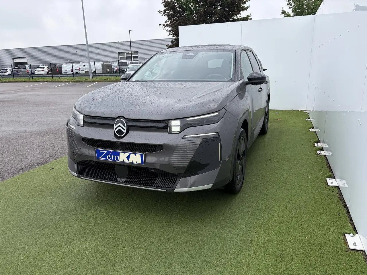Vue 3/4 avant d’un Citroën C5 Aircross 2026 gris Platinium avec toit noir et calandre distinctive sur fond vert.