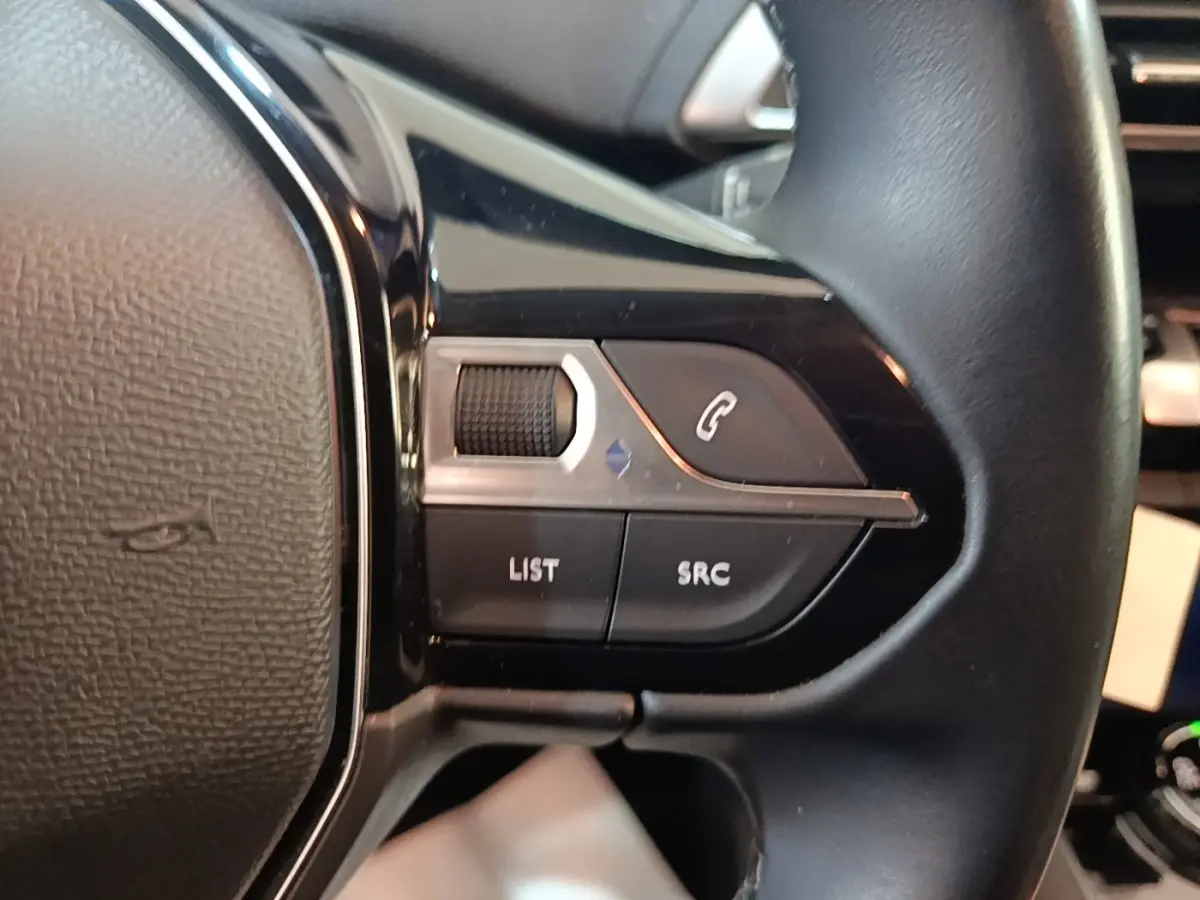 Gros plan sur les commandes gauche du volant cuir noir du Peugeot 5008, boutons pour téléphone et audio visibles.