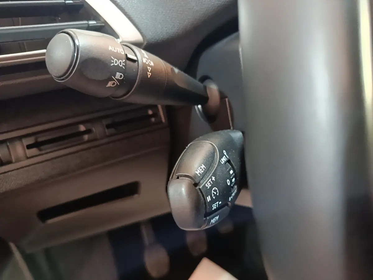 Gros plan sur les commandes au volant du Peugeot 5008 noir, mettant en valeur les boutons de régulateur de vitesse et d'éclairage.