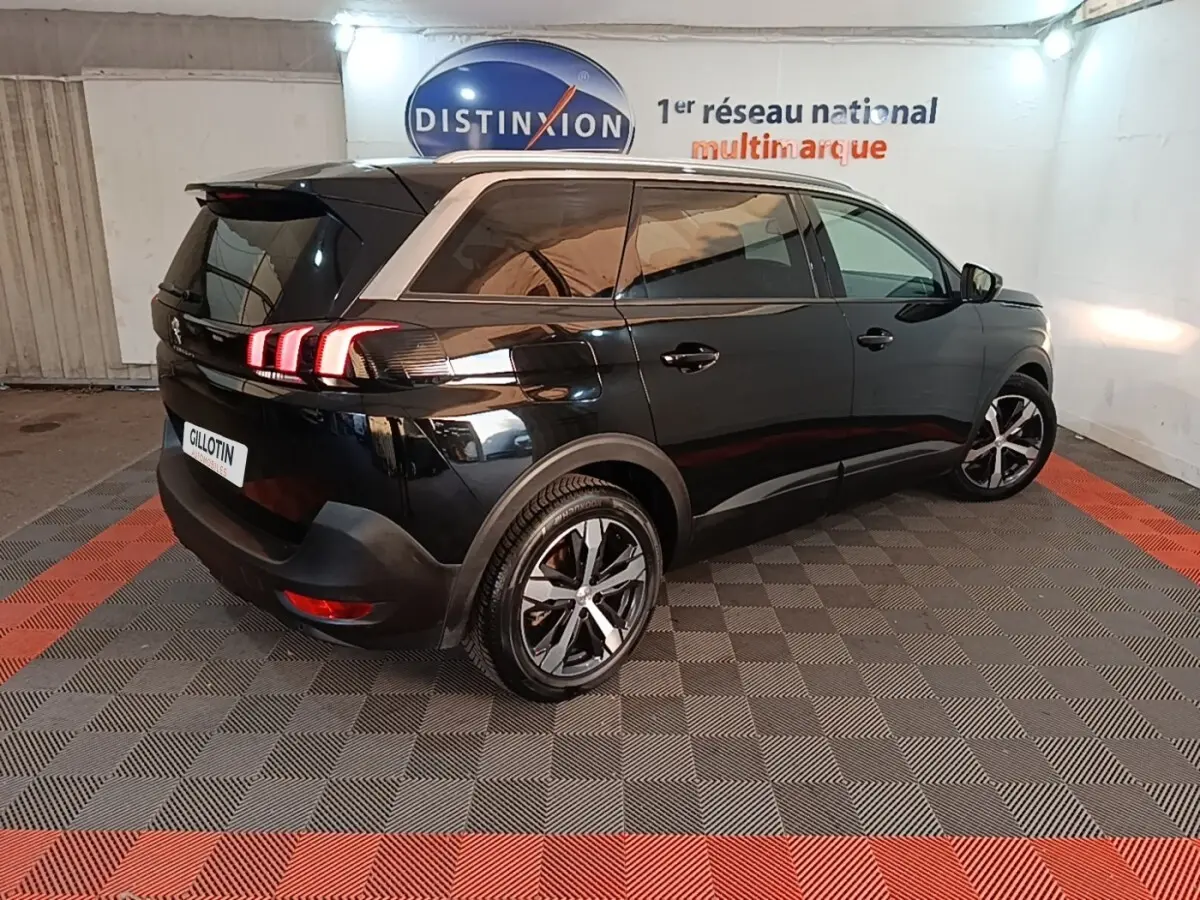 Peugeot 5008 noir vue 3/4 arrière droit en intérieur, feux arrière allumés et jantes alliage bicolores.