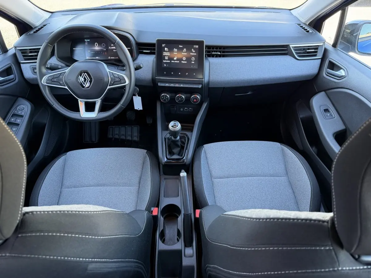 Vue intérieure avant de la Renault Clio Evolution TCe 90 2024, tableau de bord avec écran tactile central et sièges gris.