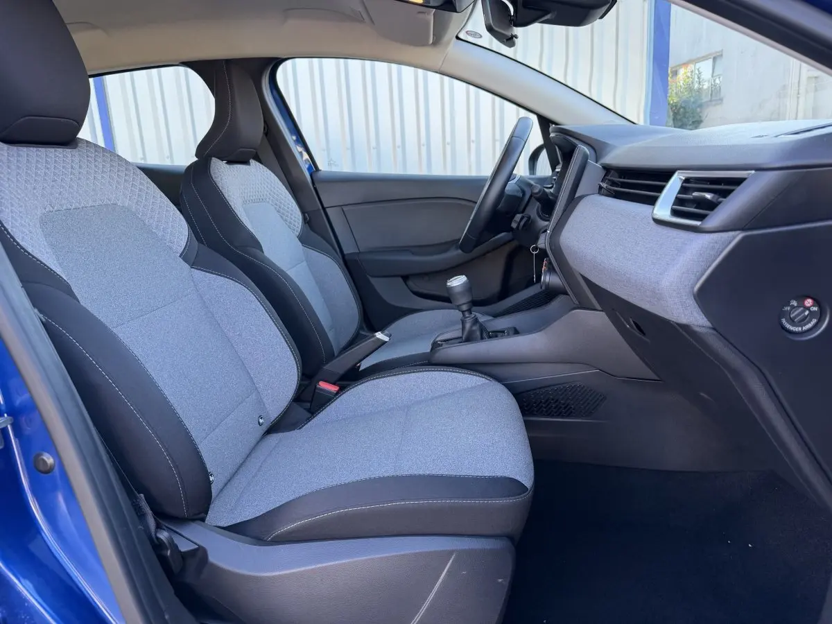 Vue intérieure côté conducteur de la Renault Clio Evolution TCe 90 2024, sièges tissu gris et noir, volant cuir et tableau de bord moderne.
