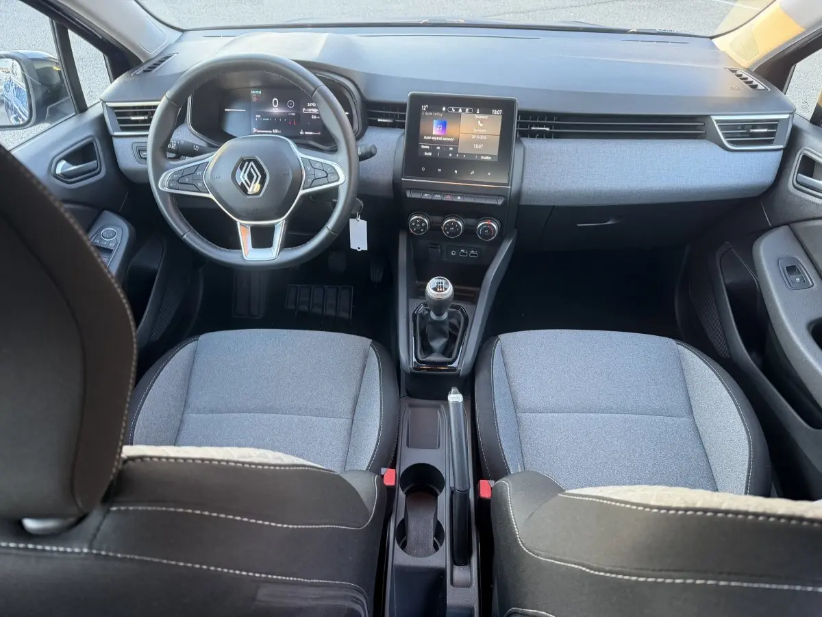 Vue intérieure avant de la Renault Clio Evolution TCe 90 2024, sièges gris, volant cuir multifonctions et écran tactile central.