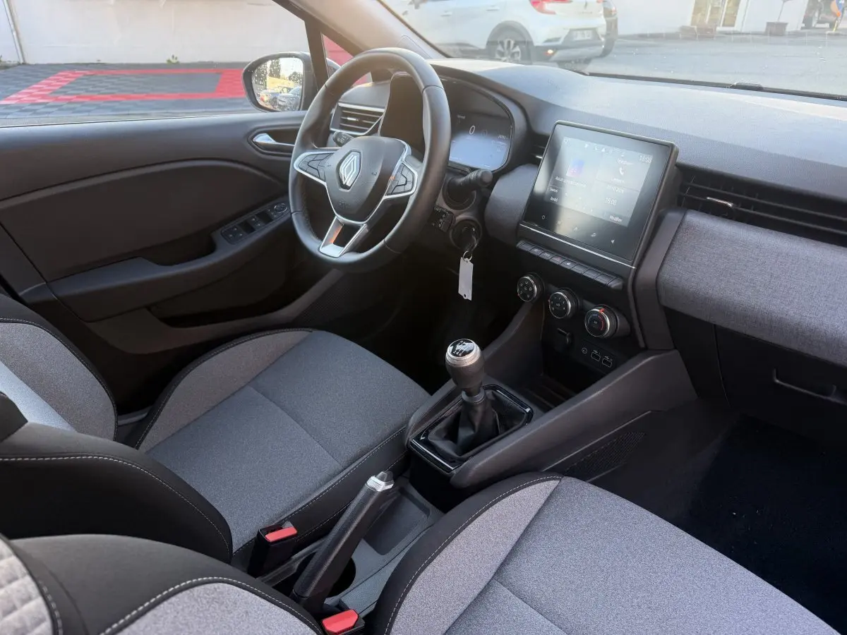 Vue intérieure côté conducteur de la Renault Clio Evolution TCe 90 2024, volant cuir, écran tactile et levier de vitesse manuel.