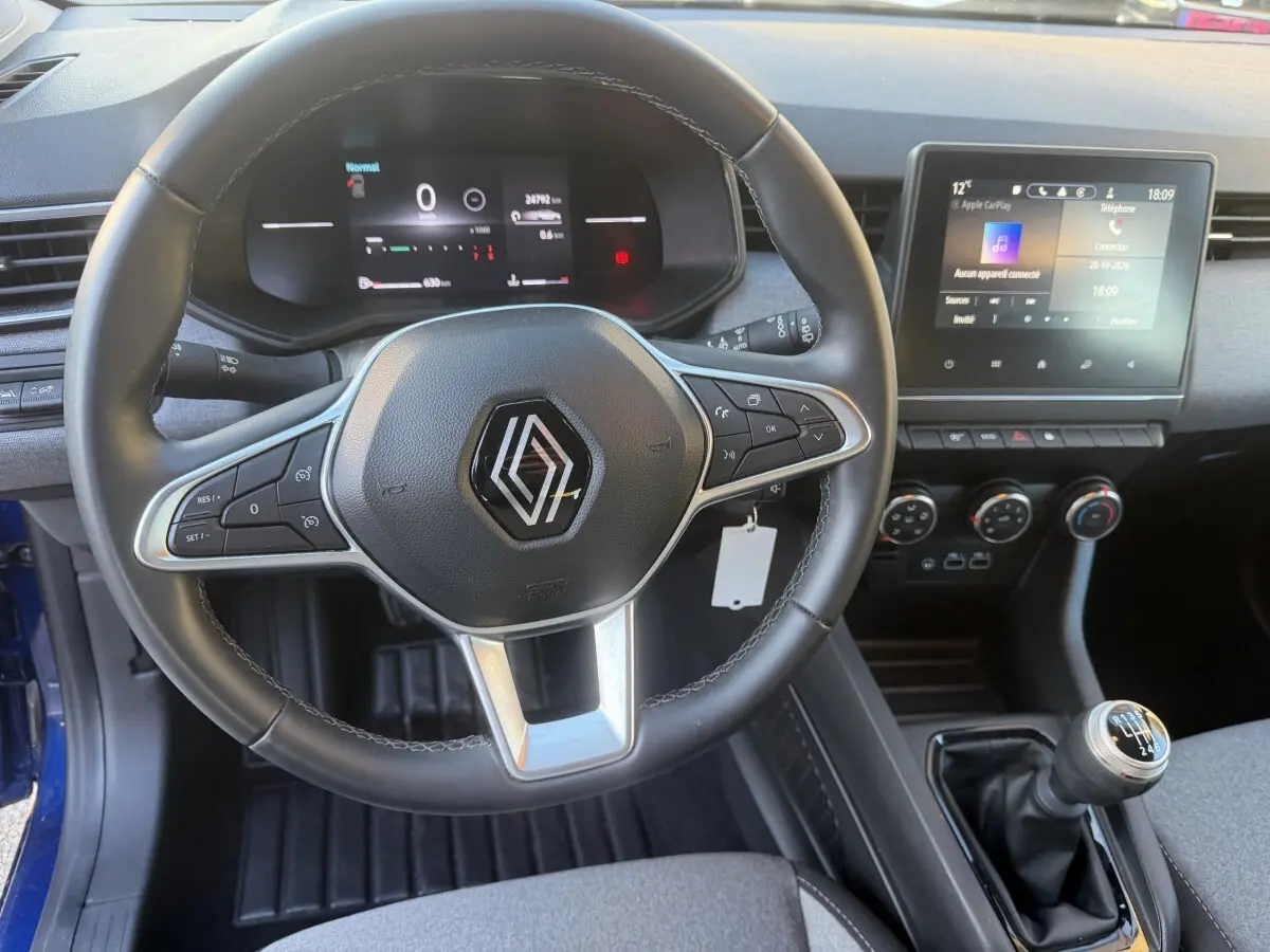 Vue intérieure centrée sur le volant cuir et le tableau de bord digital de la Renault Clio bleu 2024 avec écran tactile et boîte manuelle.