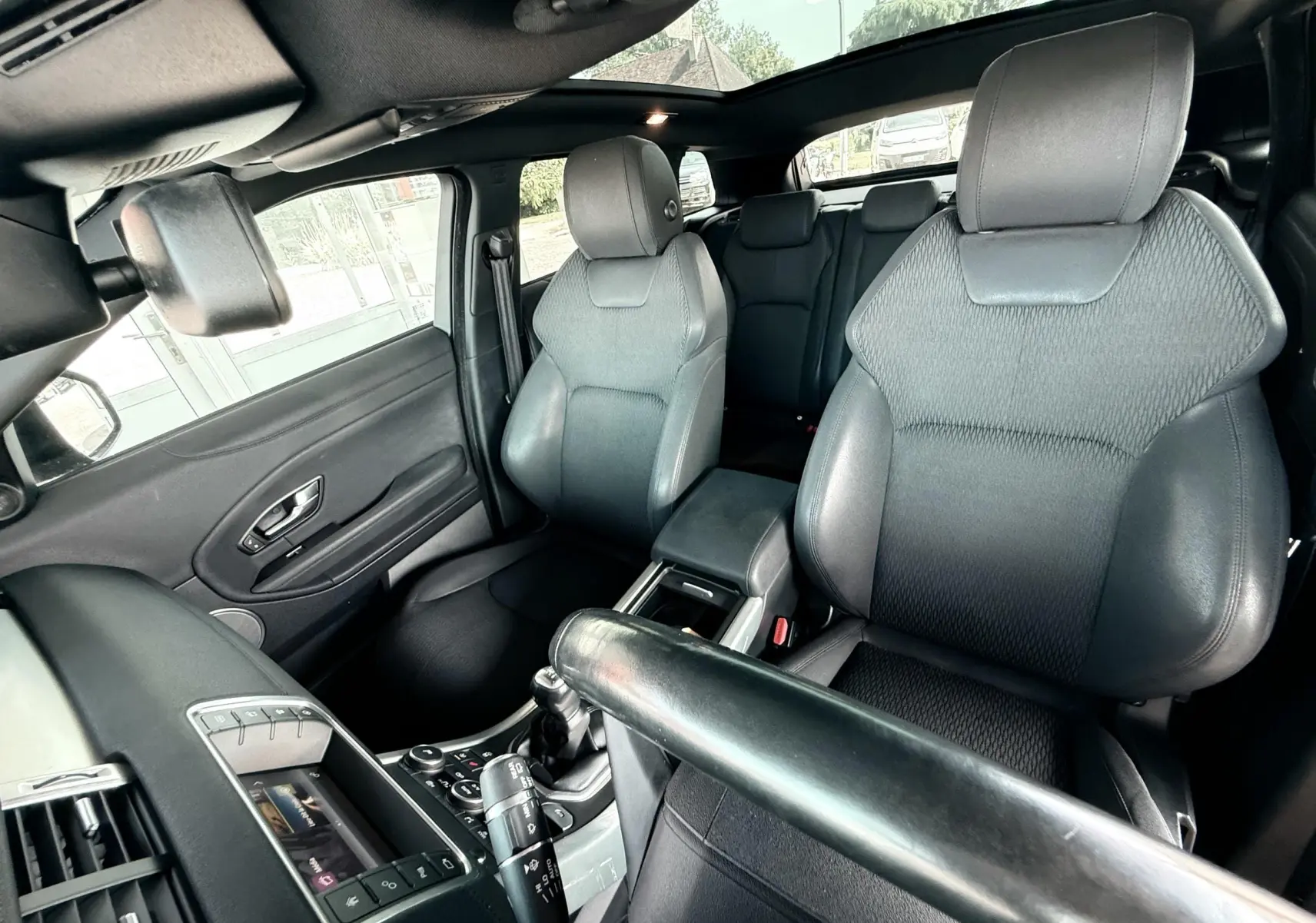 Intérieur noir du Range Rover Evoque vu côté conducteur, mettant en valeur les sièges avant et le toit panoramique.