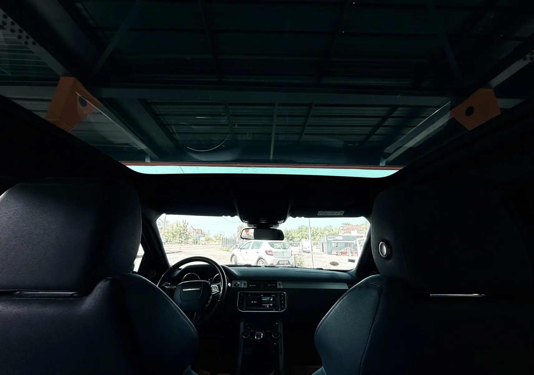 Vue intérieure du Range Rover Evoque noir 2017, montrant les sièges avant et le tableau de bord avec toit panoramique.