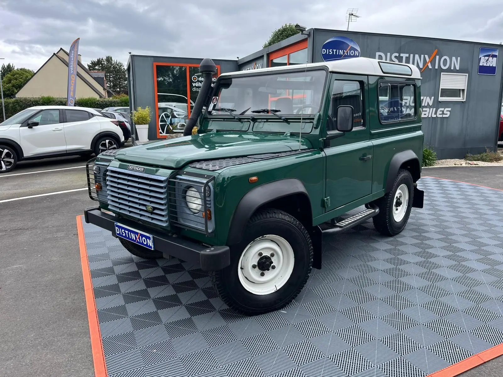 Land Rover Defender 90 vert vue 3/4 avant droit avec snorkel, marchepieds et toit blanc Hard Top.