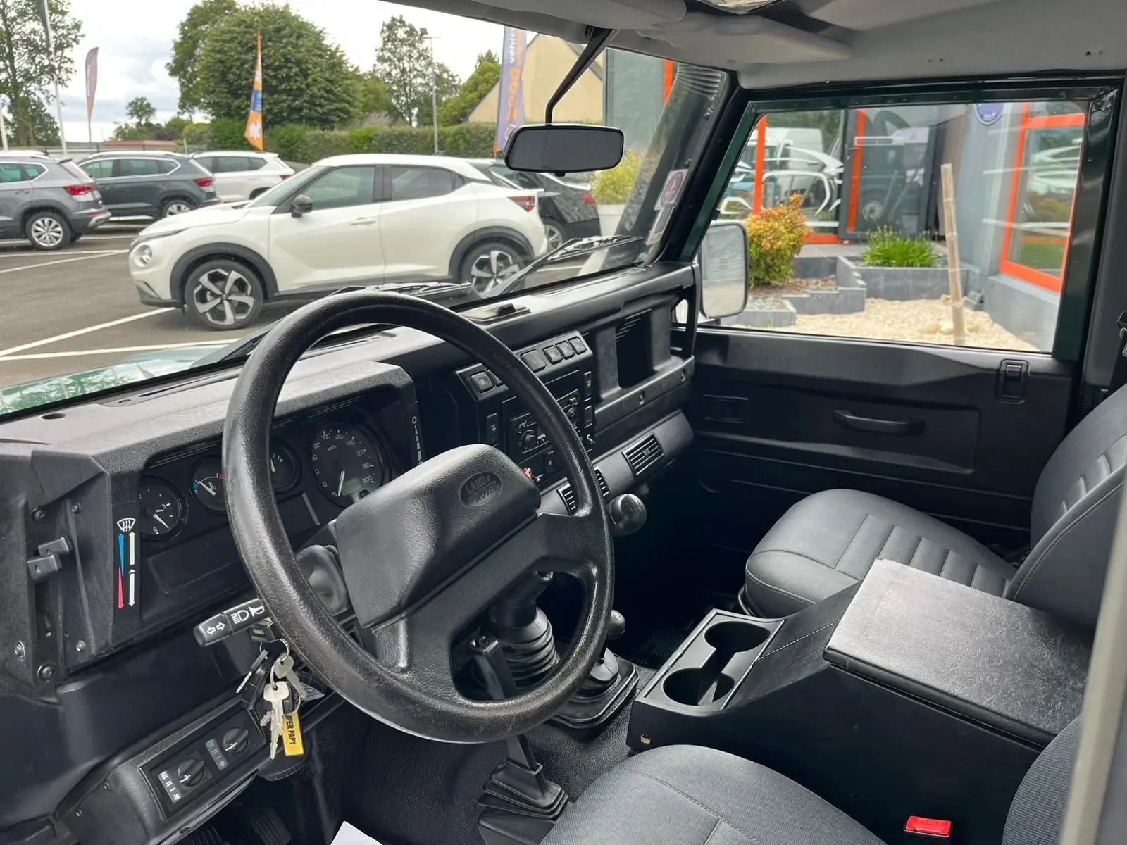 Intérieur du Land Rover Defender 90 vert de 2004, vue côté conducteur montrant le tableau de bord et la boîte manuelle.