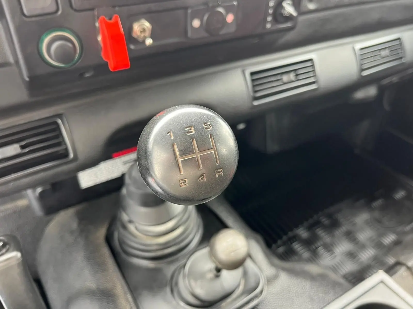 Gros plan sur le levier de vitesses manuel du Land Rover Defender 90 Hard Top vert de 2004, intérieur simple et fonctionnel.