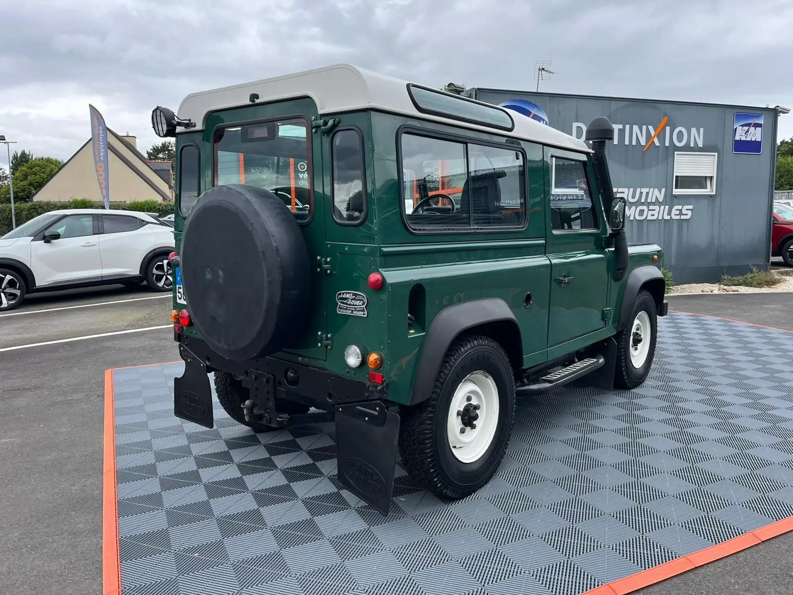 Vue 3/4 arrière droite du Land Rover Defender 90 vert avec Hard Top blanc, snorkel et marchepieds visibles.