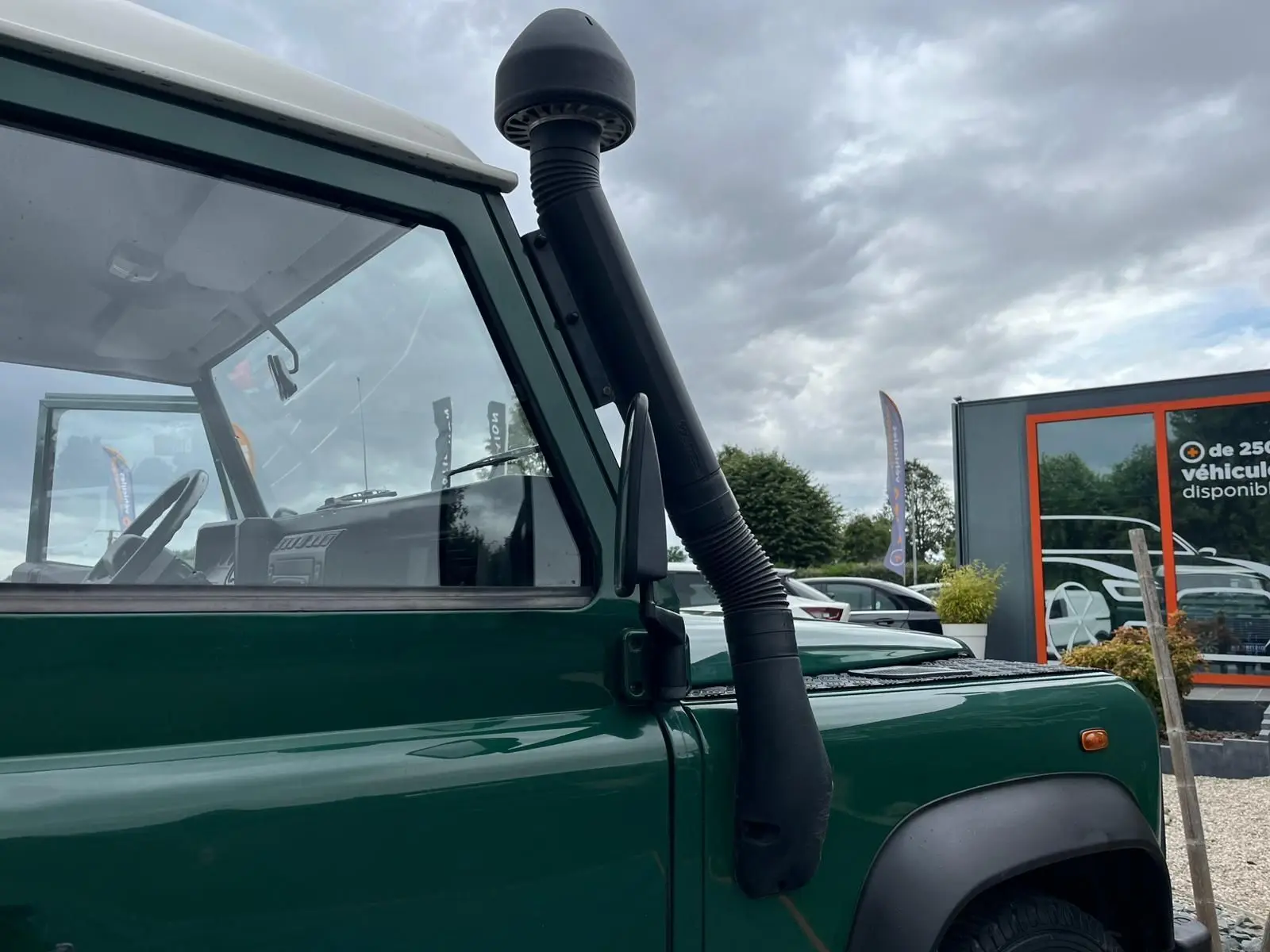 Vue latérale gauche rapprochée d'un Land Rover Defender 90 vert avec snorkel et toit dur blanc visible.